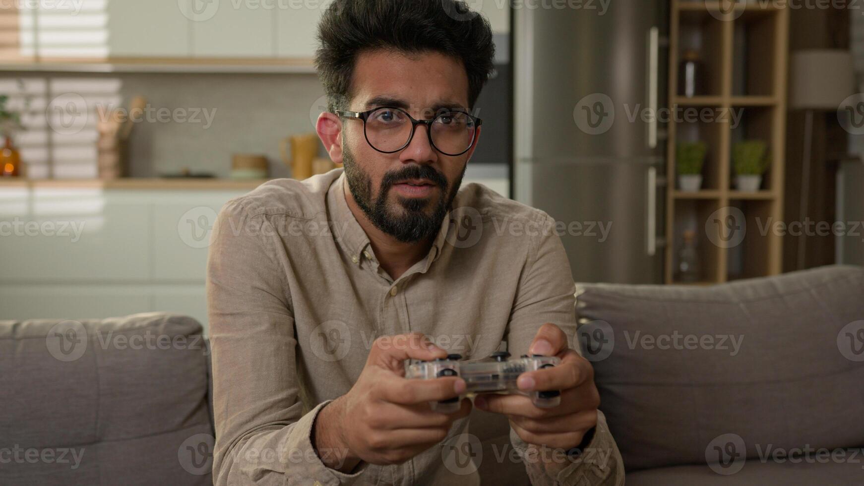 Indian Arabian man ethnic guy have fun on sofa couch play online game smart TV console virtual driving car use wireless controller entertainment in home kitchen male gamer playing with joystick photo