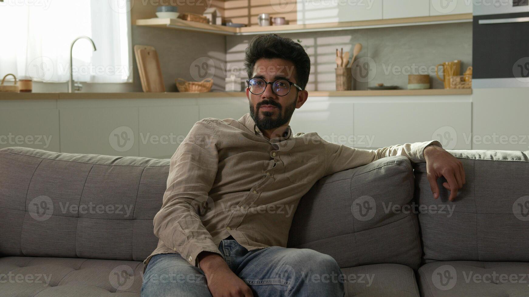 Bored unhappy tired Arabian Indian man millennial ethnic guy exhausted male homeowner relax on sofa watch television in kitchen lazy weekend watching TV channel boring rest at home couch after work photo