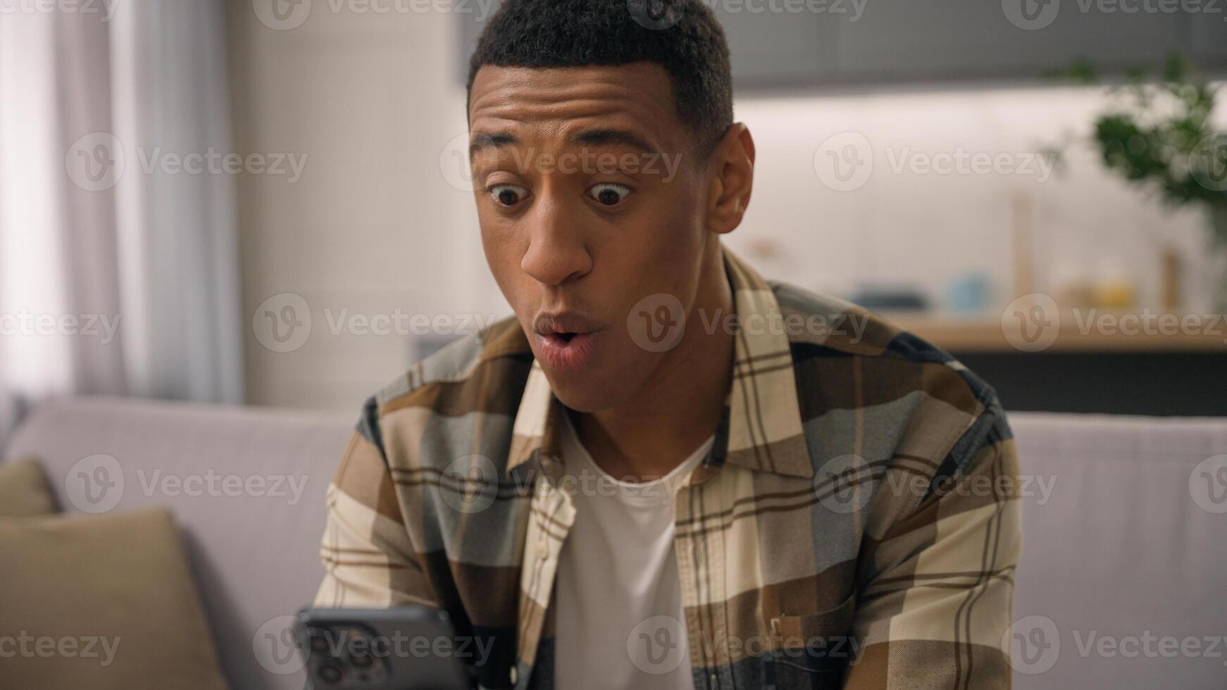 African American man say wow amazed wonder surprise reading good shocked news in mobile phone smartphone chatting browsing biracial male ethnic guy online internet shock amazing offer message at home photo