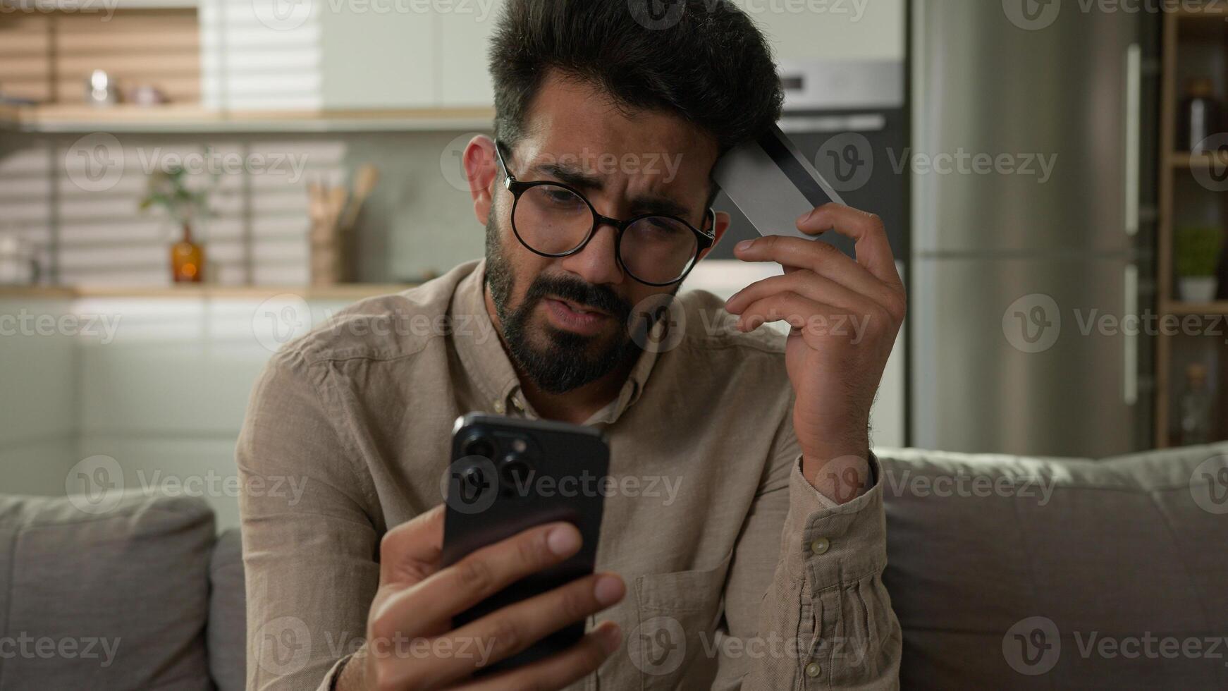 Stressed Arabian Indian man frustrated upset male cardholder pay online service with bank credit card using mobile phone disappointed banking app error no money balance lack finances financial limit photo
