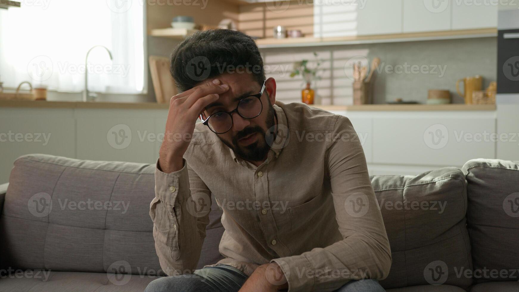 Pensive Indian Arabian man bored on home couch thinking deep in thoughts difficult decision tired exhausted thoughtful worried male boring weekend feel headache problem solution depression melancholy photo