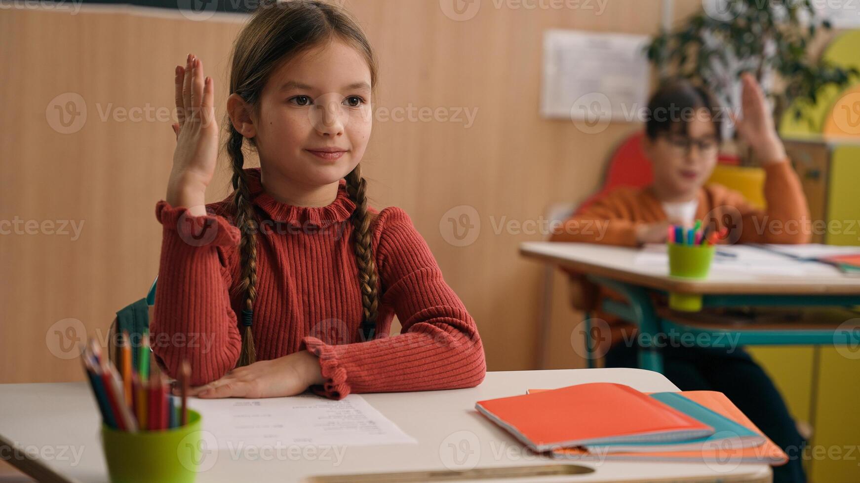 Caucasian little schoolgirl writing school class lesson rise hand answer question teacher clever smart child kid girl answering tutor boy rising arm children classmates elementary education studying photo