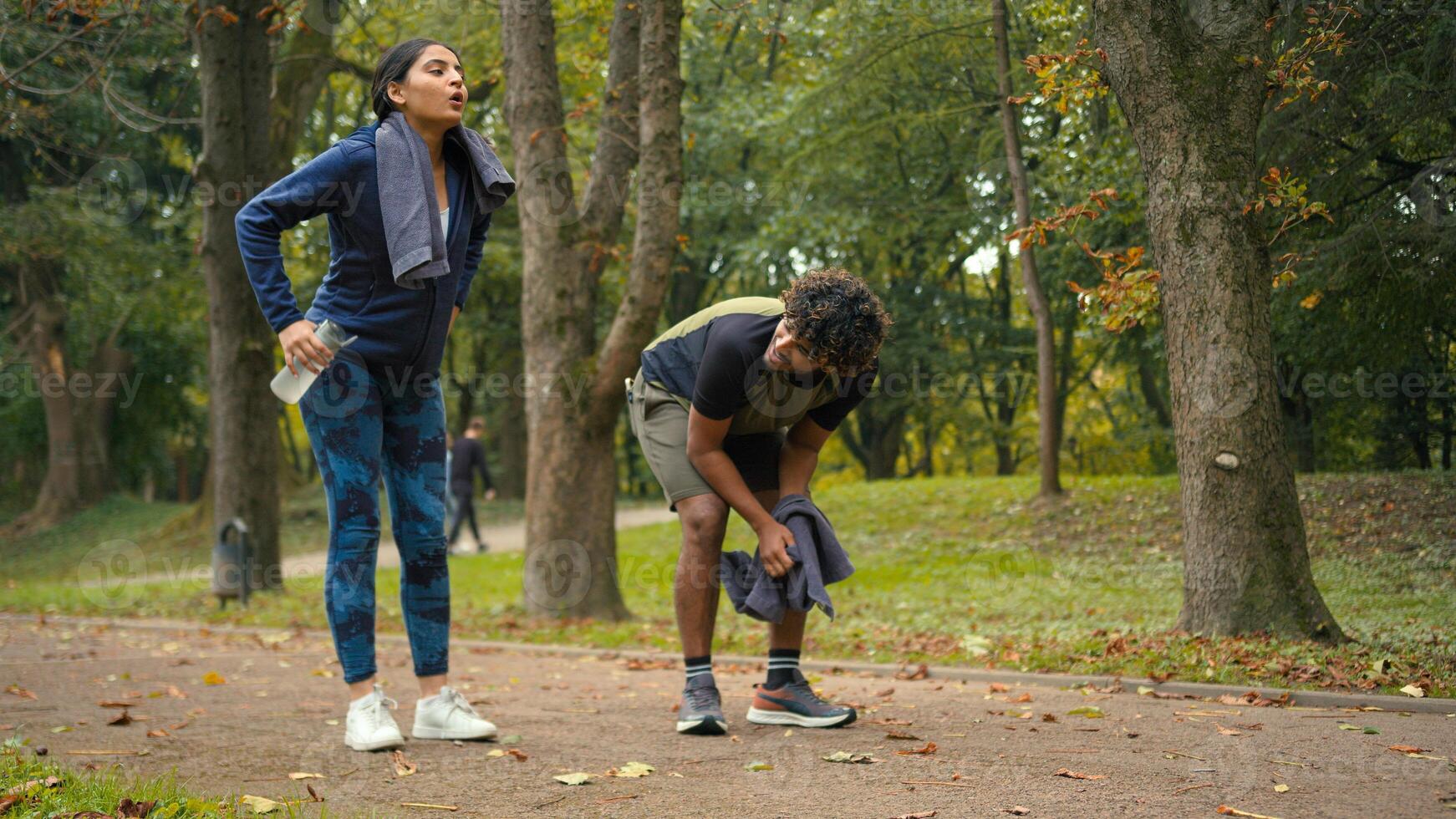 Indian Arabian couple jogging outdoors run together woman man in park stop pause break tired exhausted training activity exercise fitness runners fatigued running workout sport wipe sweat with towel photo