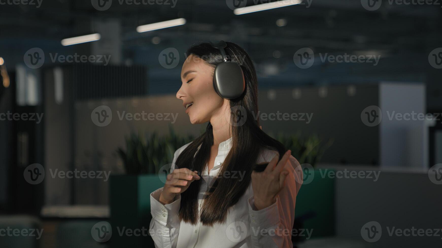Inspired Caucasian businesswoman employer office worker business woman girl manager indoors at workplace listening music in earphones headphones listen audio sing singing song enjoy break work pause photo