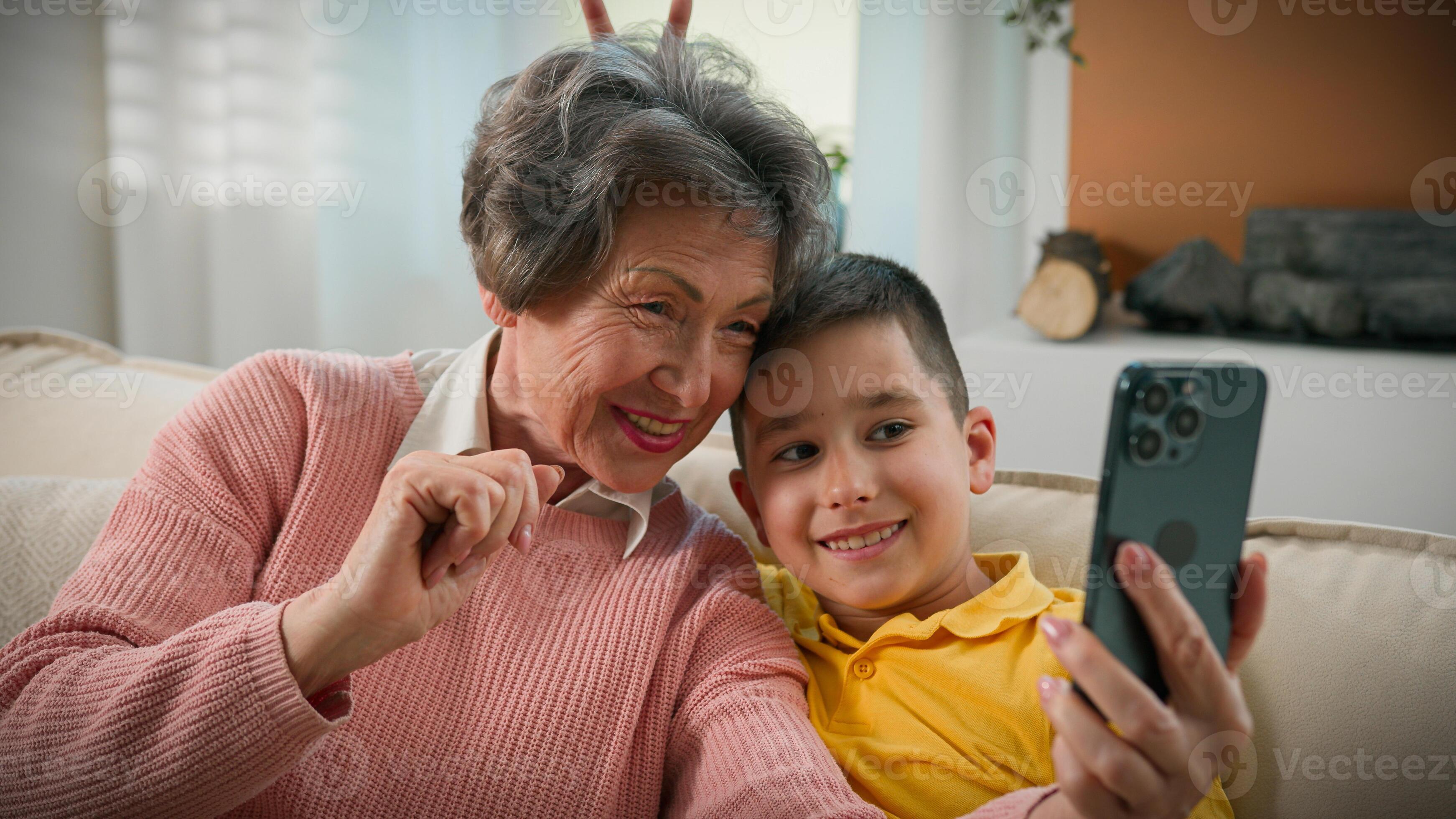 granny and boy Caucasian grandmother and grandson together at home couch photographed  selfie on mobile phone fool around funny family two generations grandma  make vlog with kid boy taking pictures using smartphone 50082613 Stock Photo