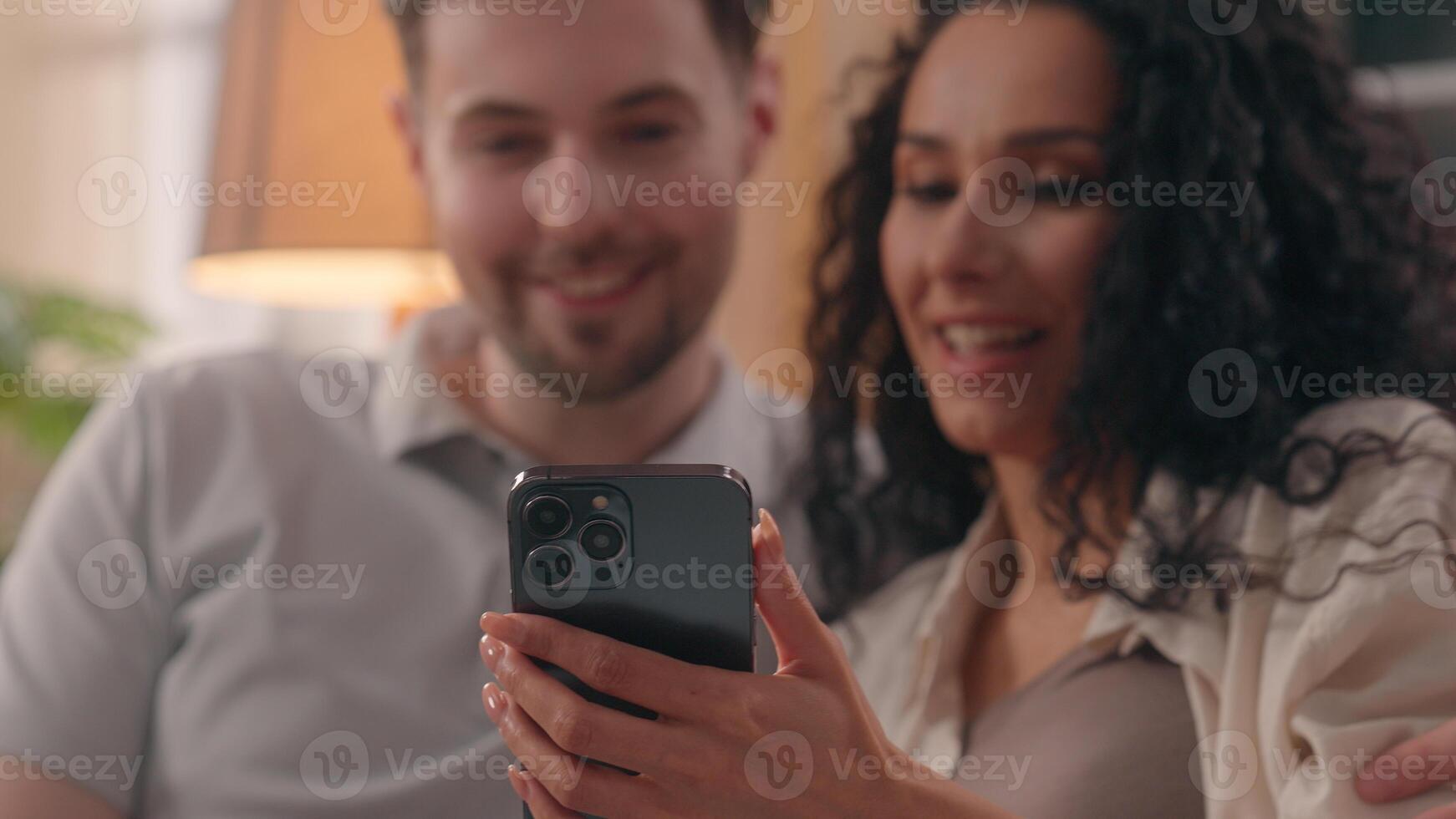 Multiracial happy couple family Caucasian man guy male Hispanic woman girl female talking using mobile phone together shopping online at home choose furniture goods purchase planning combined budget photo