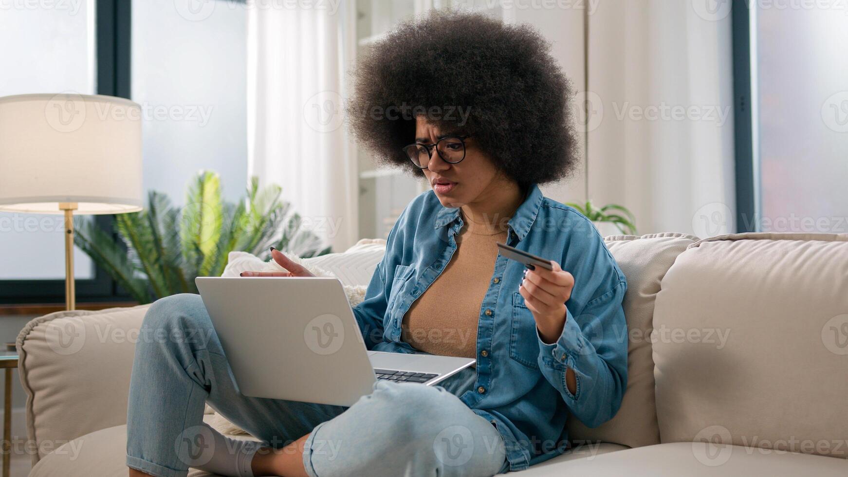 Confused puzzled irritated upset girl buyer African American woman try pay online with laptop credit card failure error mistake secure number shopping problem unsuccessful payment bank trouble at home photo