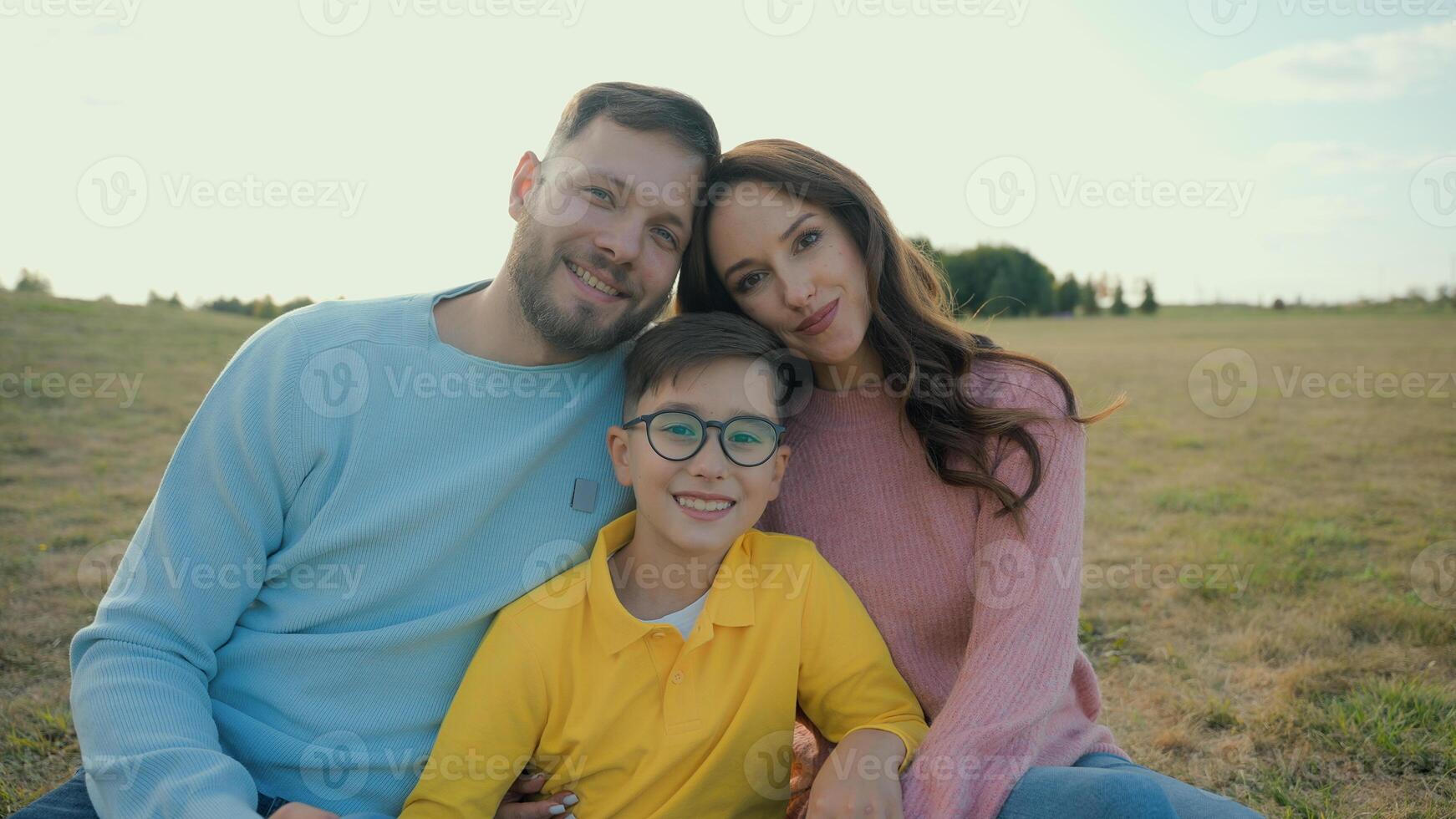 Close up portrait happy Caucasian loving family smiling parents mother father adopted little joyful boy child son kid hugging together looking at camera outside field country meadow. Adoption custody photo