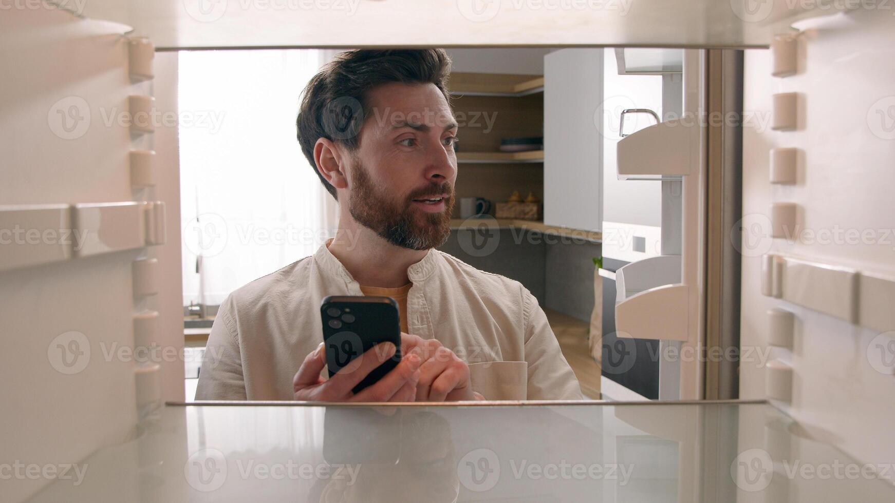 Hungry man guy open empty refrigerator poor crisis order food delivery with smartphone online buying products ordering goods with mobile phone store cellphone app point of view POV from inside fridge photo