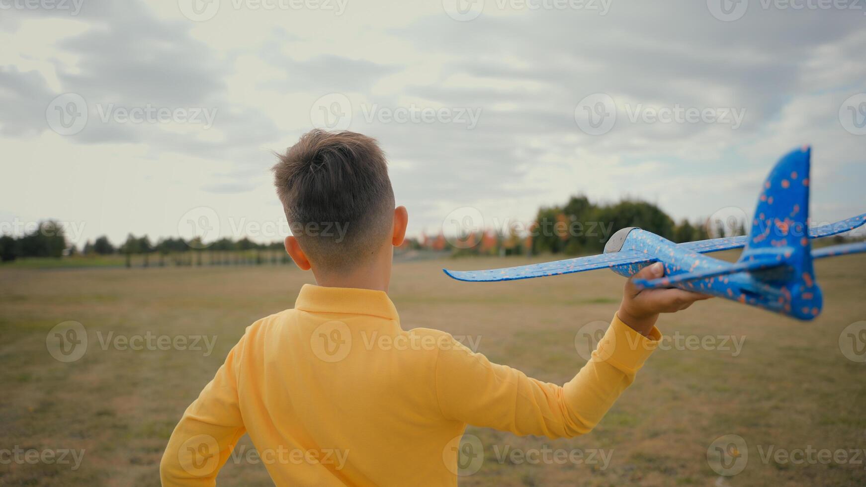 Back view adorable kid Caucasian little boy son schoolboy jog teen play with toy plane outdoors beautiful nature park field. Child playing run throw launching flying airplane flight dream become pilot photo