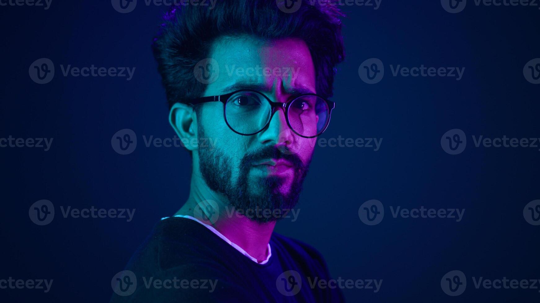 Close up male portrait in neon ultraviolet blue background Indian man Muslim Arabian guy posing in profile turning head looking at camera with serious face expression hacker developer coding worker photo