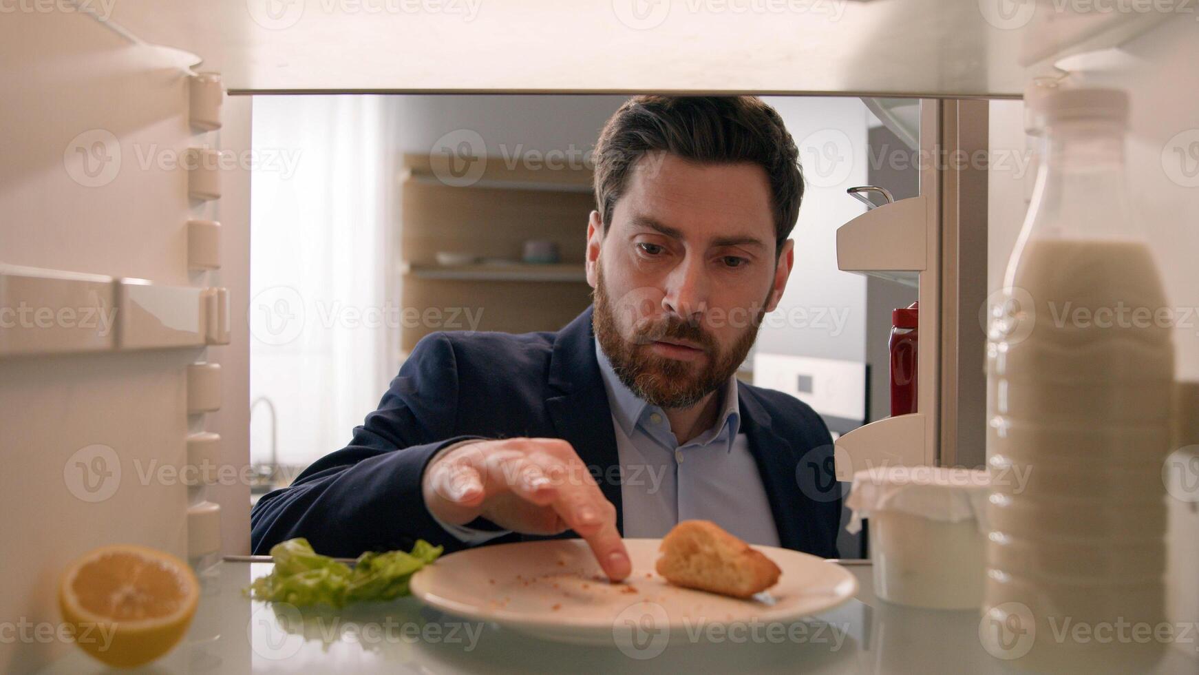 Hungry adult Caucasian businessman entrepreneur man after work open empty refrigerator with half lemon, lettuce leaf, bottle of milk and slice of bread eat crumbs POV point of view from inside fridge photo