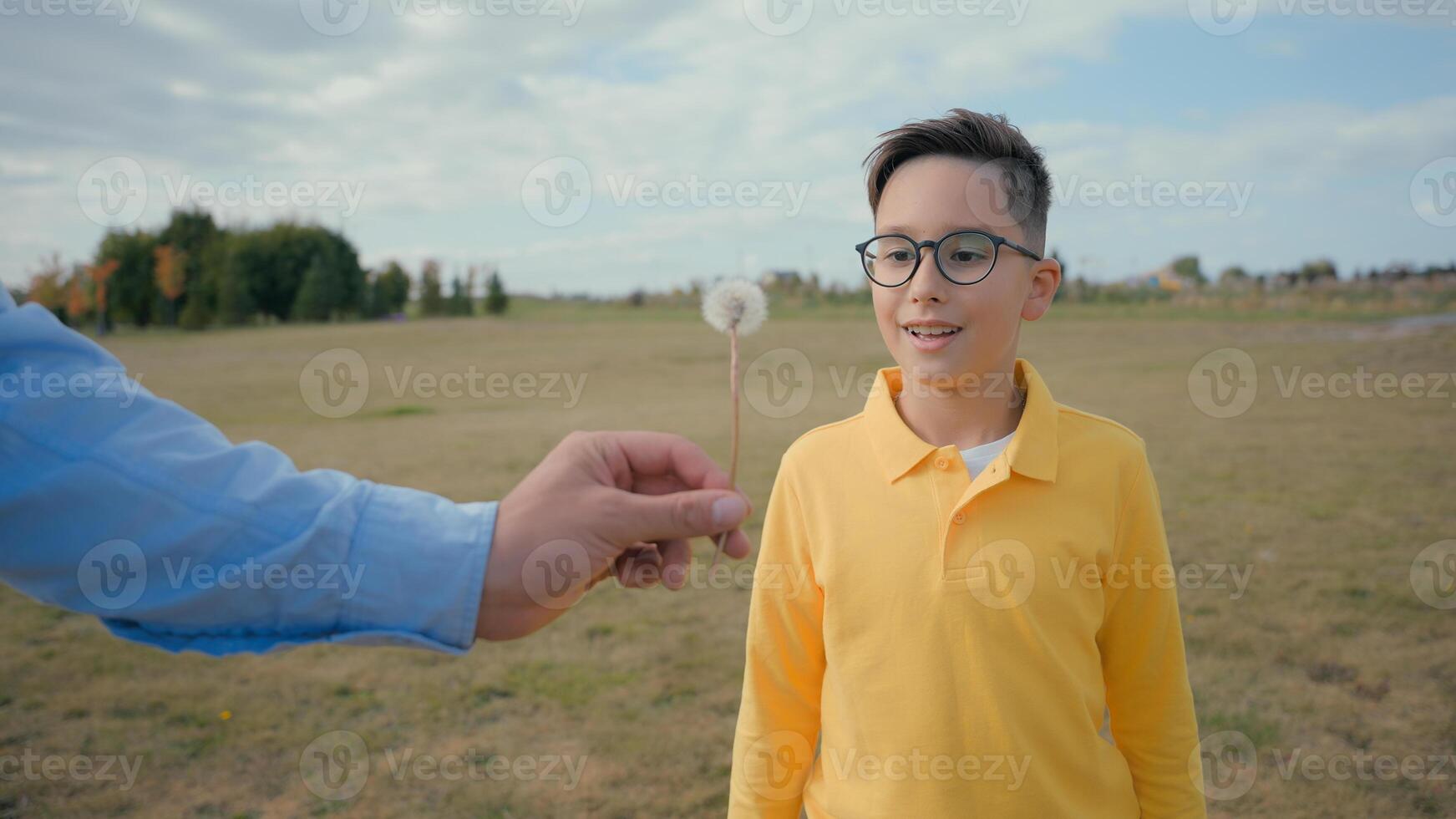 Happy smiling joyful Caucasian child little boy kid having fun blowing dandelion air unrecognizable parent hand hold flower play outside field country meadow. Ecology nature environmental care village photo