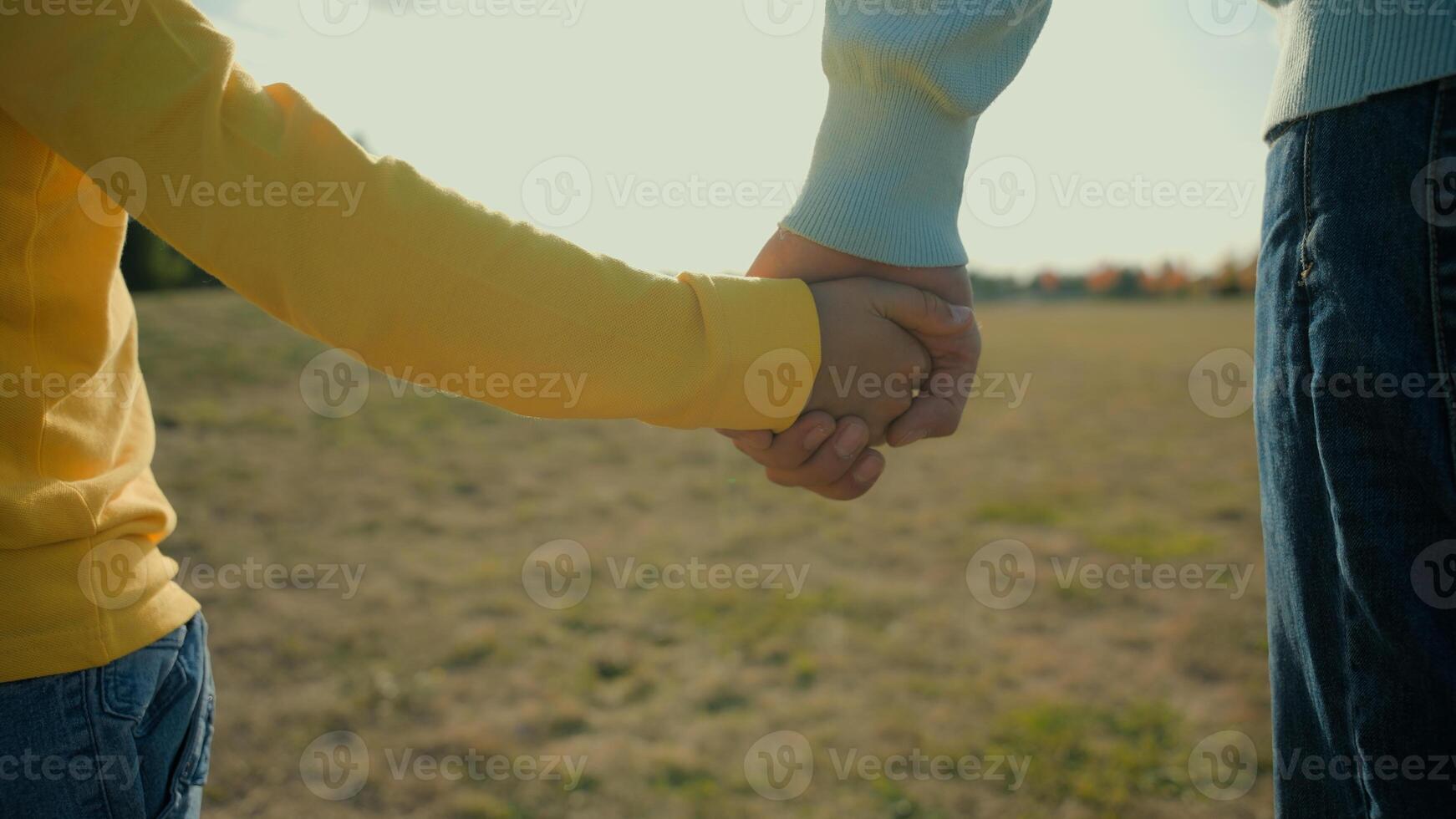 Little unrecognizable Caucasian boy adopted child kid son schoolboy holding hands together unity support gesture hand hold father male foster parent dad man stepdad happy family outside nature meadow photo