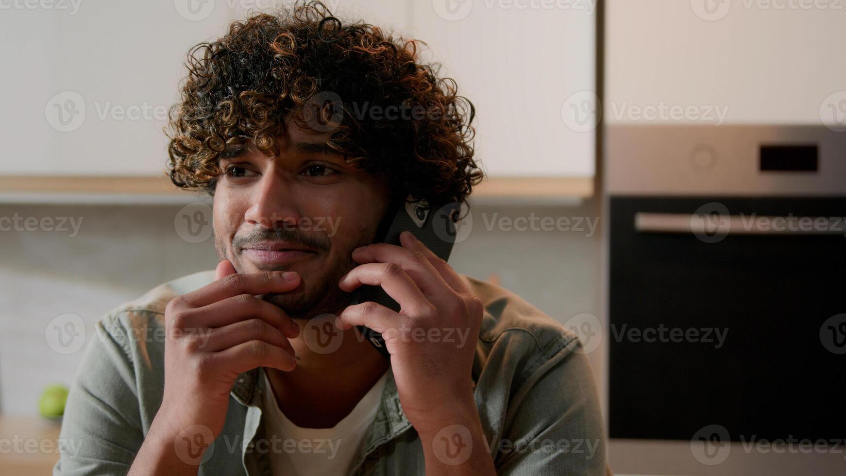 Happy smiling Indian man carefree positive talking mobile phone at home answer call friendly talk laughing smile funny casual communication discuss Arabian guy speak smartphone conversation at kitchen photo