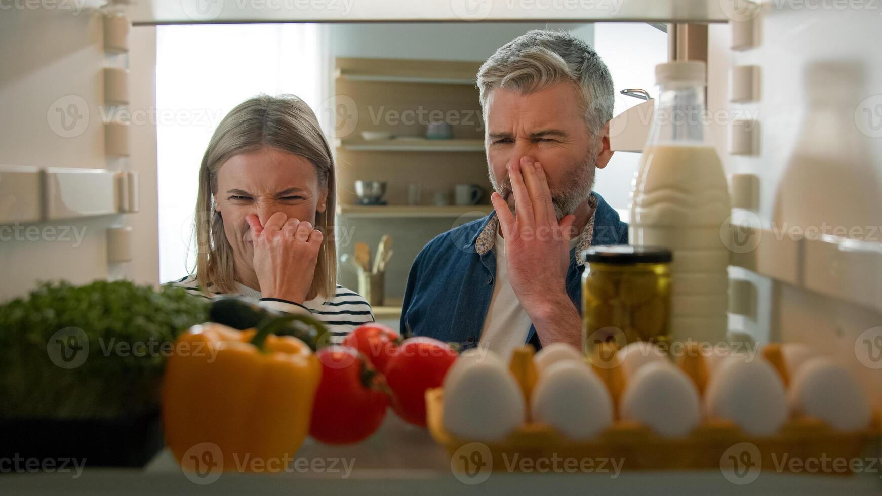 POV Point of view from inside fridge adult couple feeling bad disgusting unpleasant smell from broken refrigerator spoiled rotten food meal middle-aged man and woman awful smelling stink from freezer photo