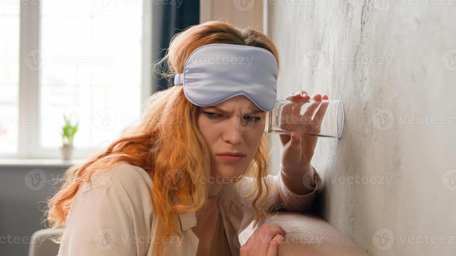 Shocked angry girl leaning to wall in bedroom at early morning curious Caucasian woman overhearing noisy neighbor using glass listening neighbors quarrel shock eavesdrop neighborhood eavesdropping photo