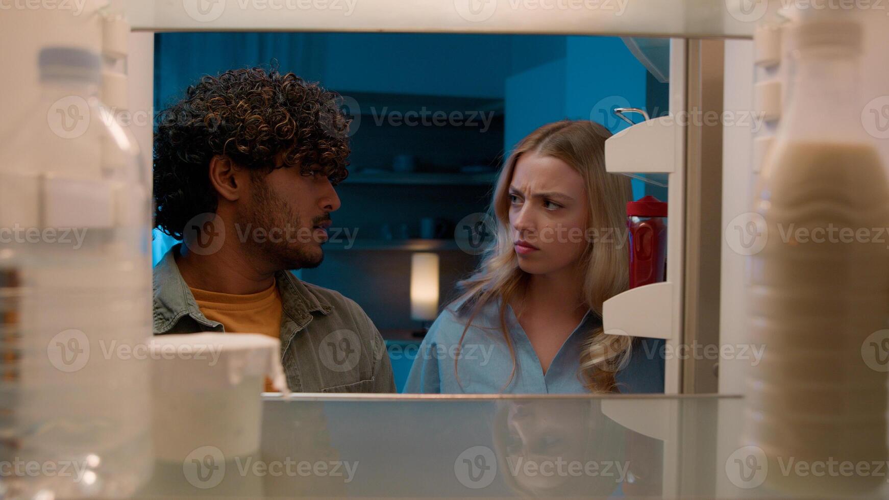 Point of view POV inside refrigerator Caucasian girl woman girlfriend wife and Arabian man Indian guy boyfriend husband multiracial couple at night evening open empty fridge at kitchen unhappy sad photo