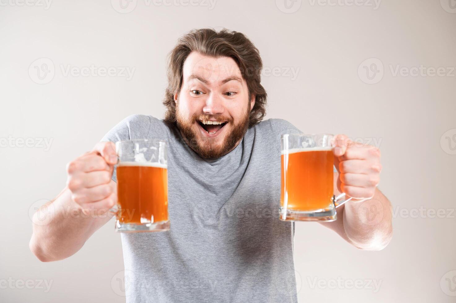 Portrait of a happy young bearded man holding two beer mugs isolated over light gray background photo