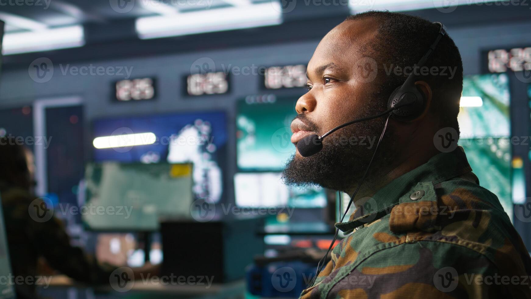 Military dispatcher using headphones microphone, offering information to commanders fighting on front lines. Army expert providing intel for troops in base of operations, camera B photo