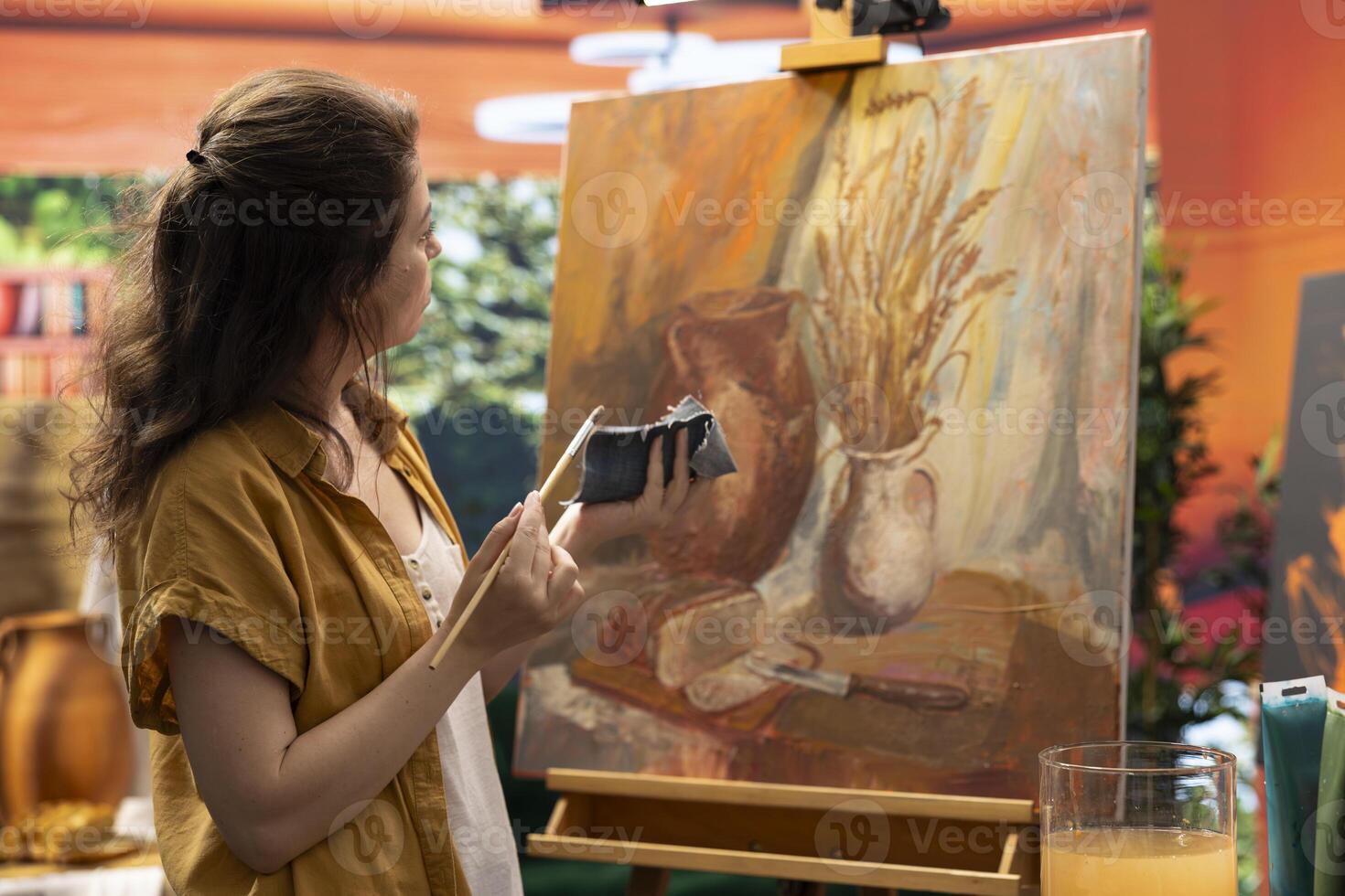 Woman artist wiping off a color from her paintbrush before mixing oil paints, creating a multicolored rustic artwork with paint tubes. Painter showing her talent and creativity in art studio. photo