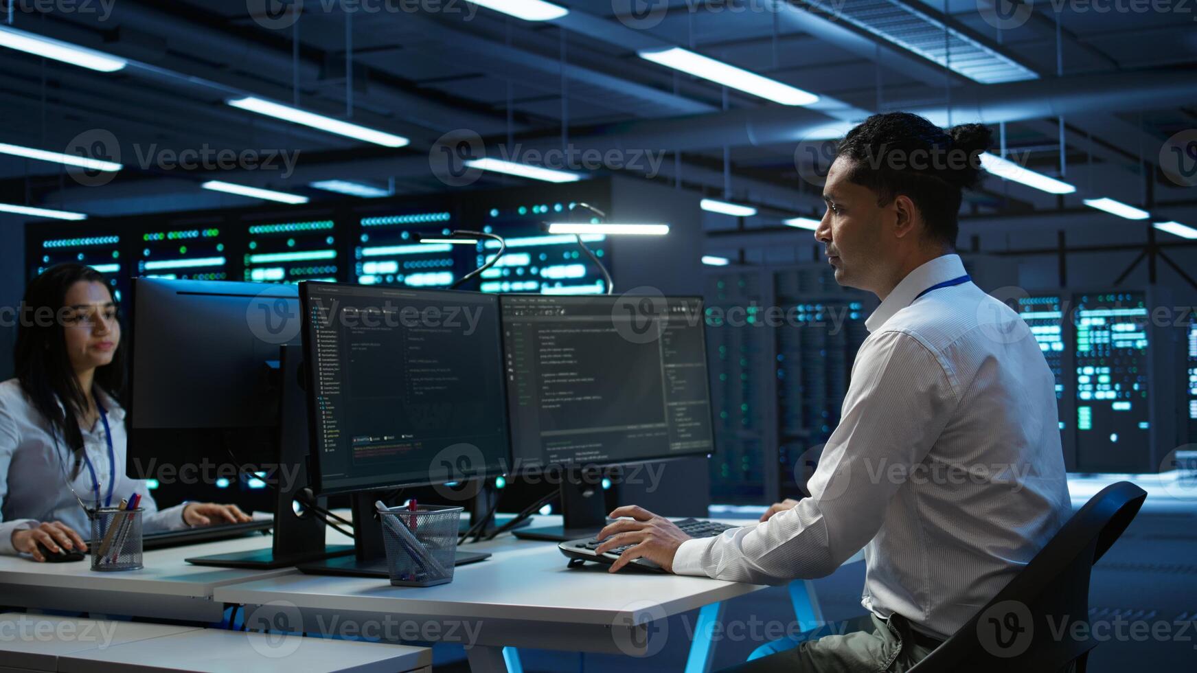 Engineer overseeing data center, making improvements and updates to ensure system can handle networking tasks, handheld camera shot. Indian man in server room tracking network traffic, camera B photo
