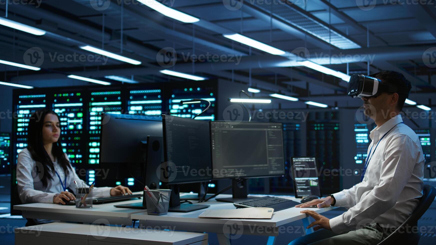 Admin in data center using virtual reality tech to ensure system can handle networking tasks. Server room worker wearing VR headset to track network traffic with PC, making improvements, camera B photo
