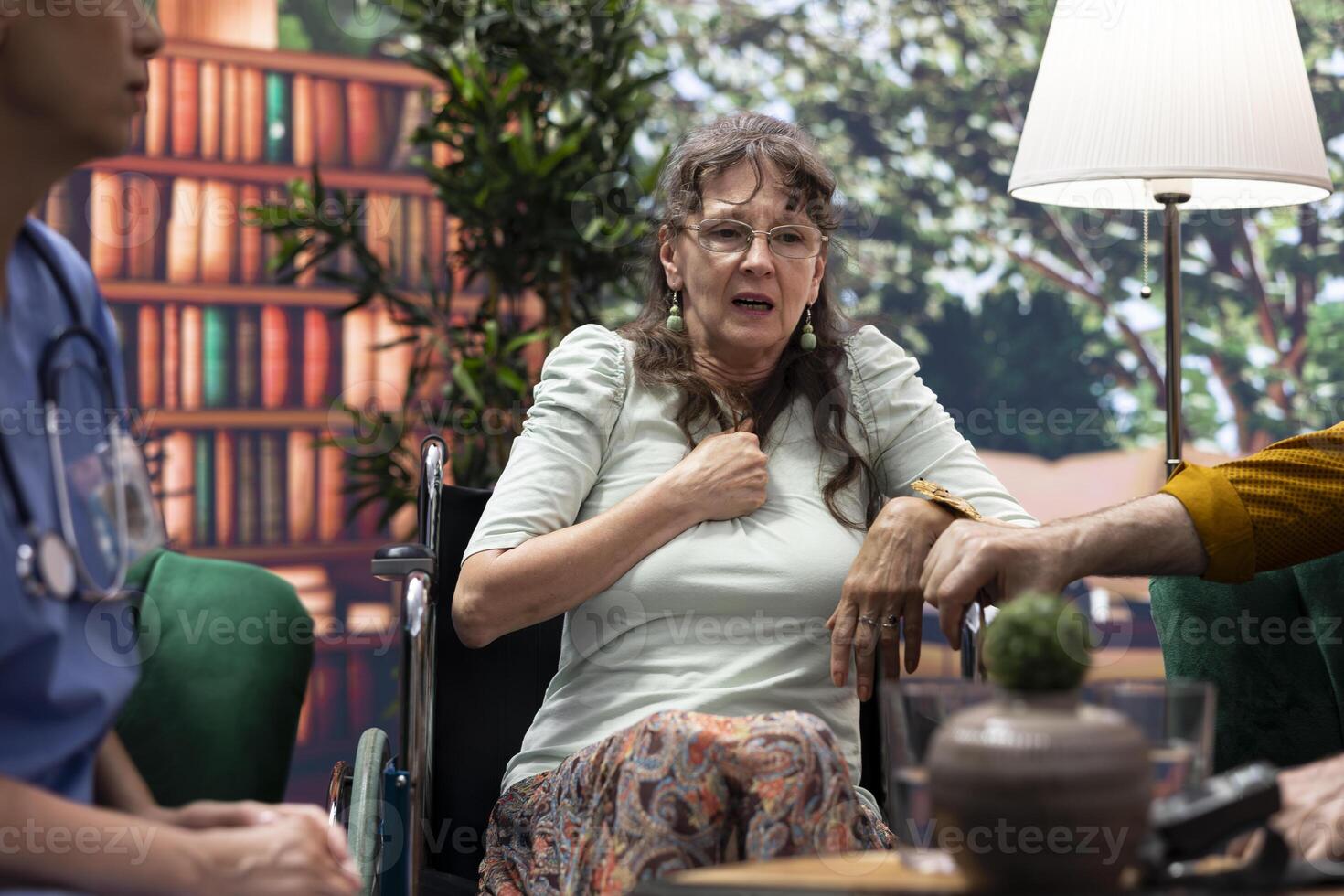 Caregiver chatting with elderly woman with disability during home visit, recommending medicine and supplements to help with recovery. Nurse and senior wheelchair user in a consultation. photo
