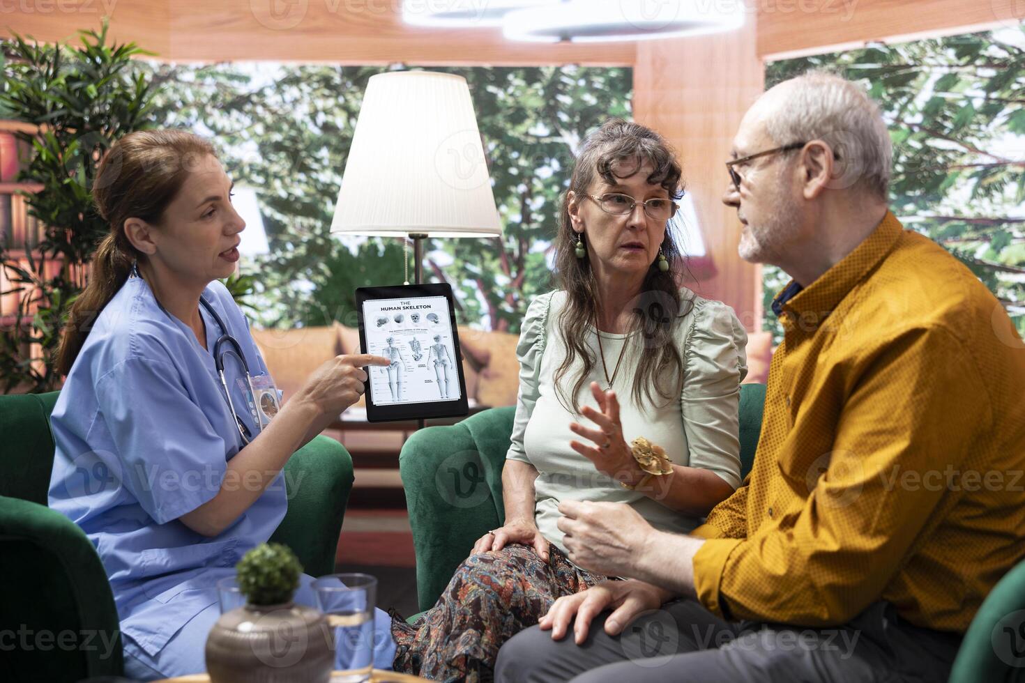 Orthopedic specialist explaining osteopathy disease diagnosis on tablet, presenting the human skeleton for a bones examination. Nurse discusses with senior patients about osteochondrosis. photo
