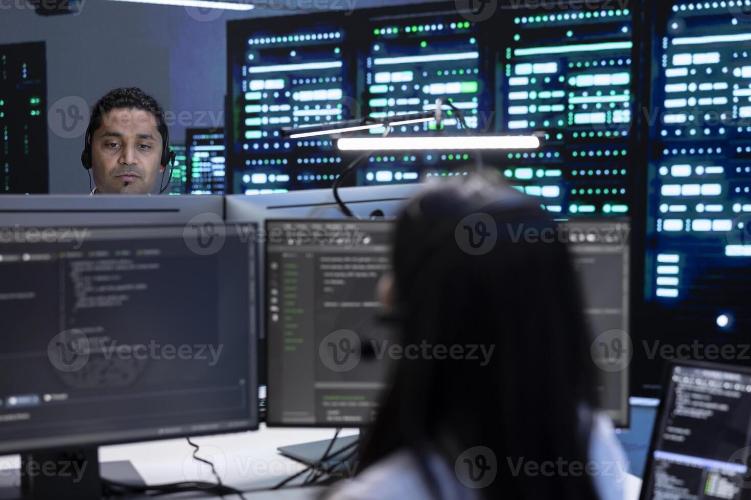 Team of professionals in data center supporting engineering team doing equipment maintenance, talking in headset microphone. Teamworking colleagues in server farm coordinating technicians using mic photo