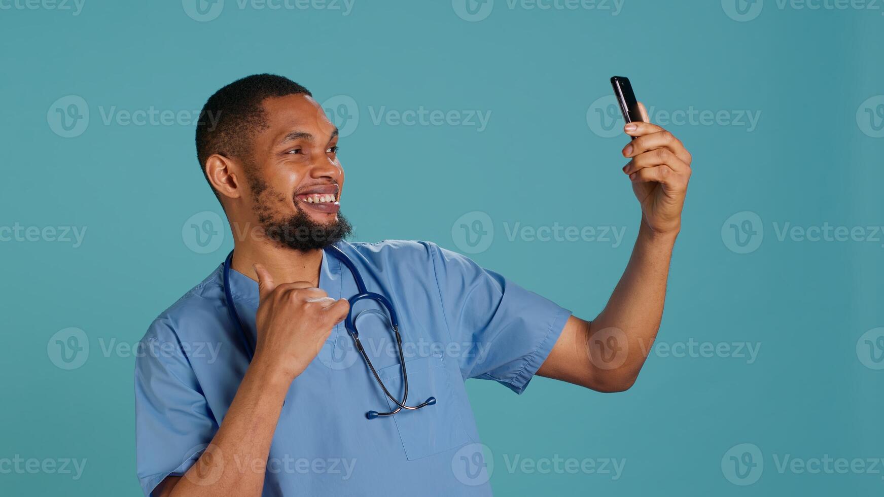 Male nurse using mobile phone to take selfies during hospital job shift break. Healthcare worker using smartphone to take pictures of himself, isolated over studio background, camera A photo