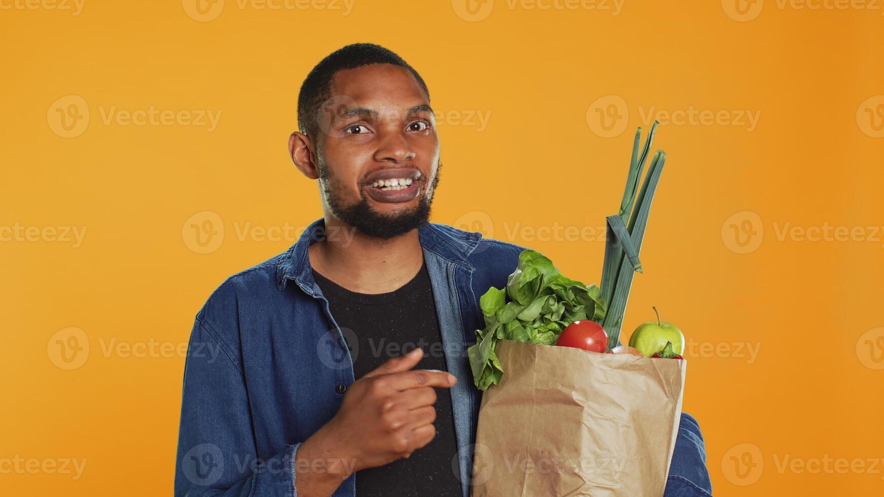 African american person pointing at ethically sourced fruits and veggies stored in a paper bag, making eco friendly recommendations for healthy eating and vegan nutrition. Camera A. photo