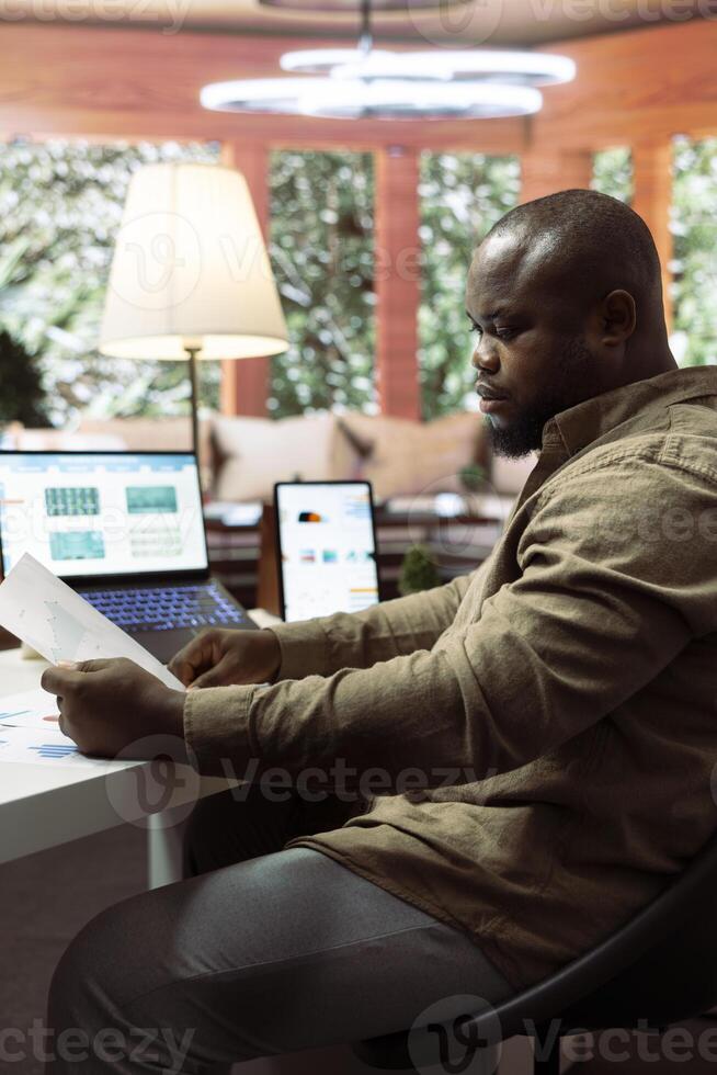 Entrepreneur explores potential business expansion plans on laptop, studying statistics and data visualizations documents. Enterprise owner works to boost profit and earnings. photo
