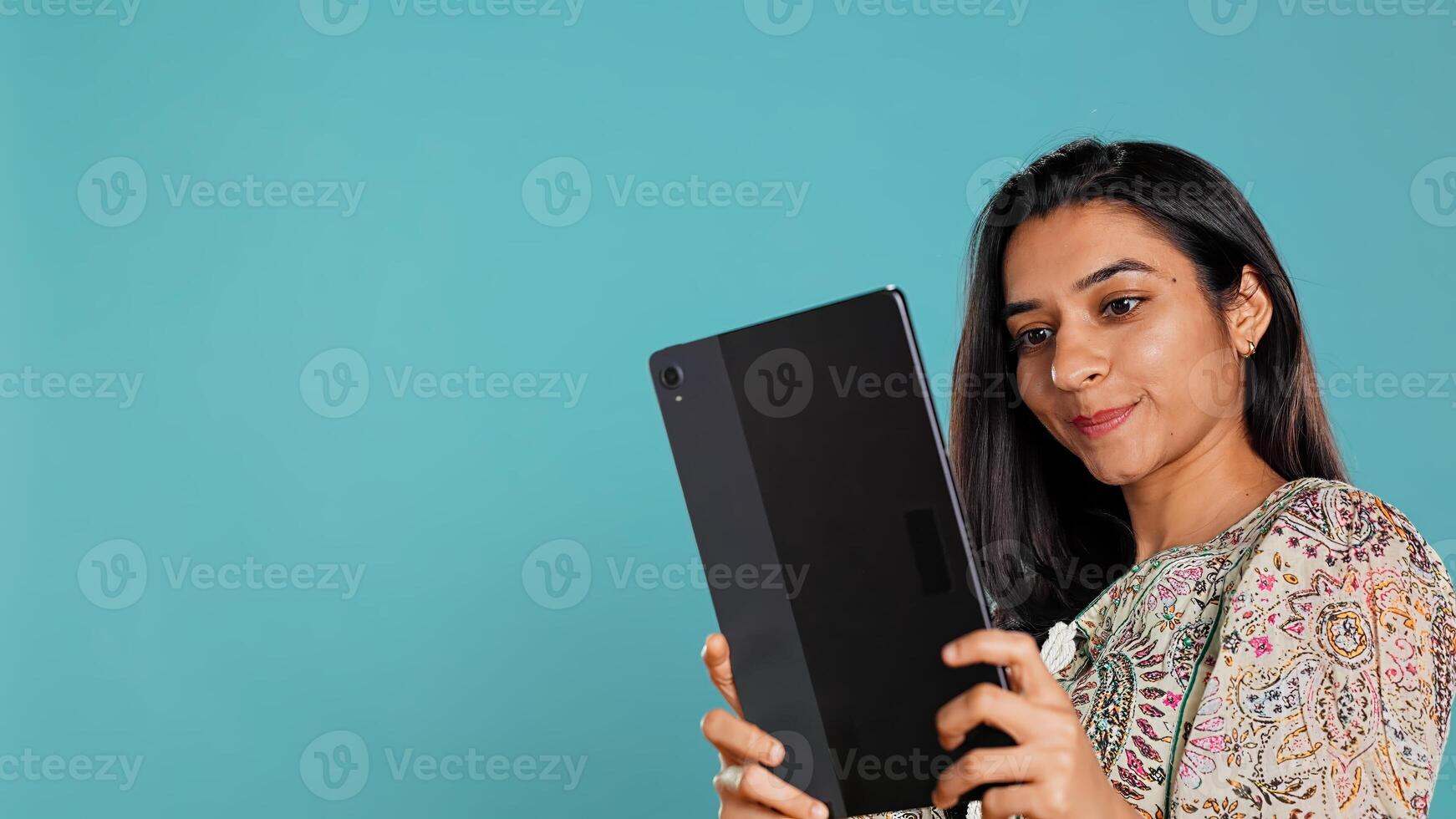 Indian narcissistic woman using tablet to take selfies from all angles. Vain social media user taking photos using digital device selfie camera, smiling happily, studio background, camera B