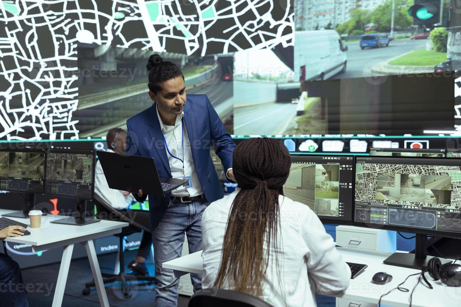 Indian man instructing his employees in using CCTV surveillance system to help couriers with directions and gps coordinates. Shipping agency working on express delivery service, satellite map. photo