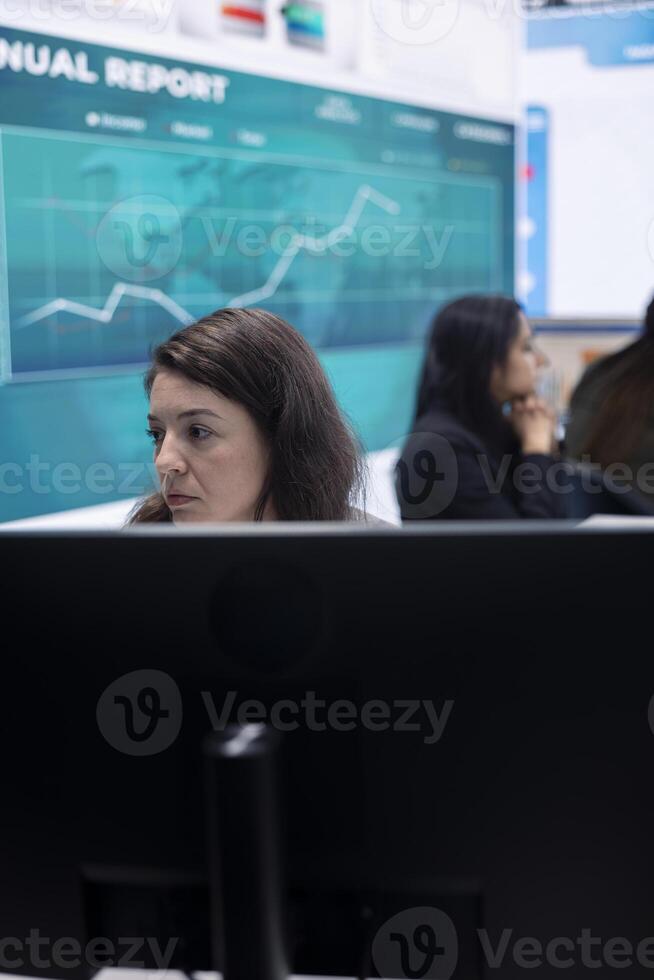 Marketing specialist studying infographics on computer in a monitoring room with big screen, check customer satisfaction from annual data reports. Employee review performance metrics. photo