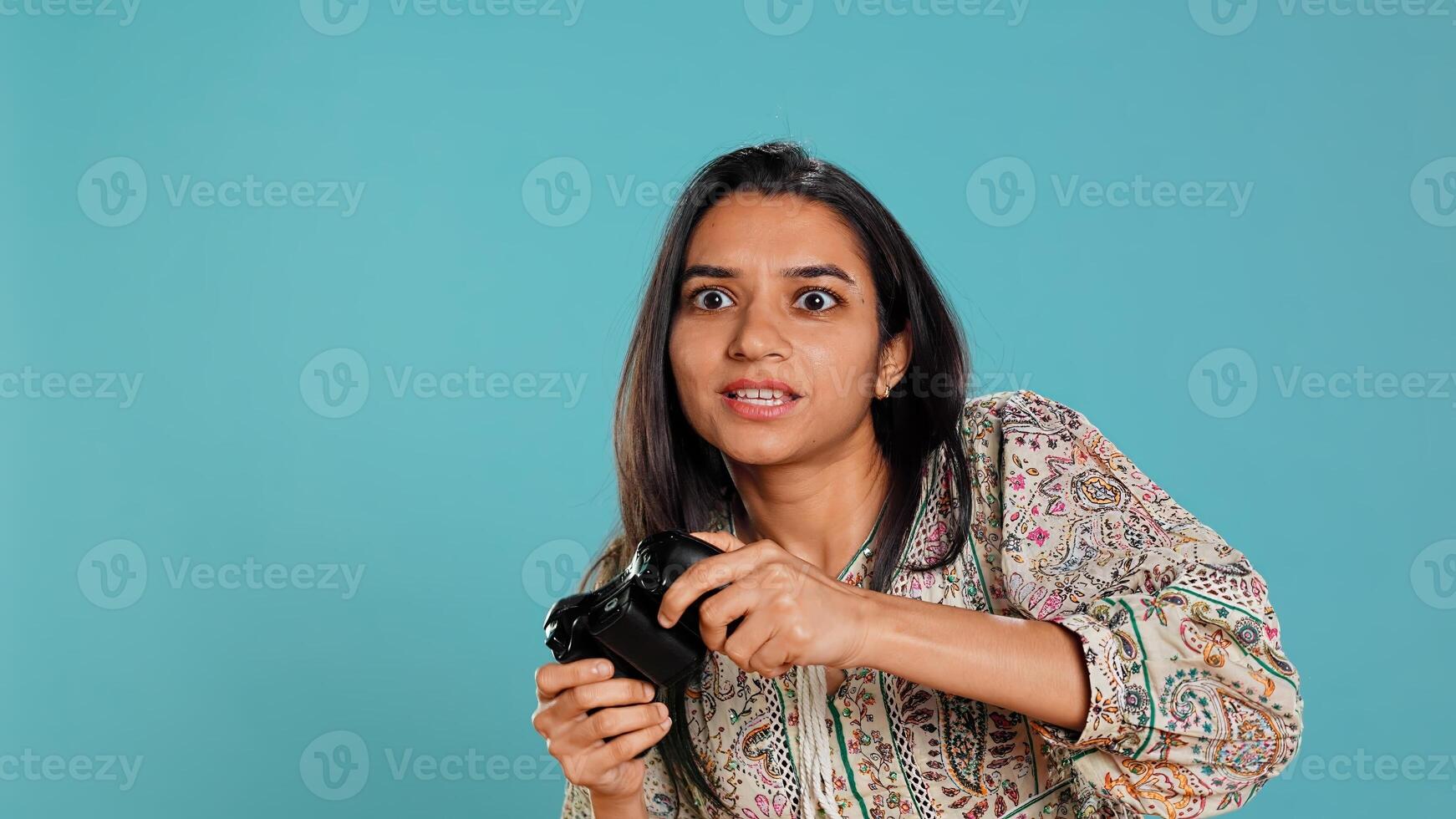 Jolly gamer celebrating after winning game on gaming console, studio background. Delighted Indian woman bragging after being victorious in videogame, defeating all enemies using gamepad, camera B photo
