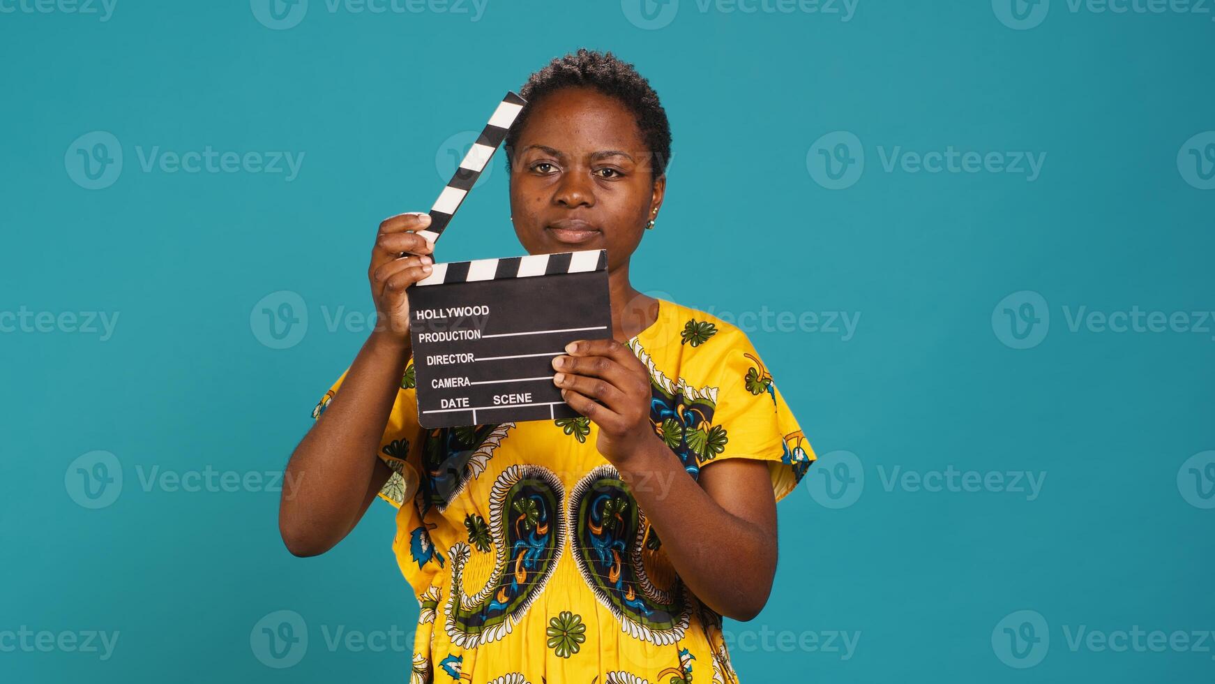 Young woman movie producer clapping filming slate to cut a scene, saying action and using a clapperboard for cinema industry. Filmmaker uses clapboard against blue background. Camera A. photo