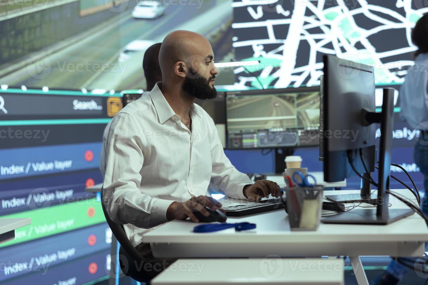 Middle eastern employee monitors couriers in the field and giving directions to avoid heavy traffic, locating delivery trucks around town via CCTV footage. Man handles cargo logistics. photo