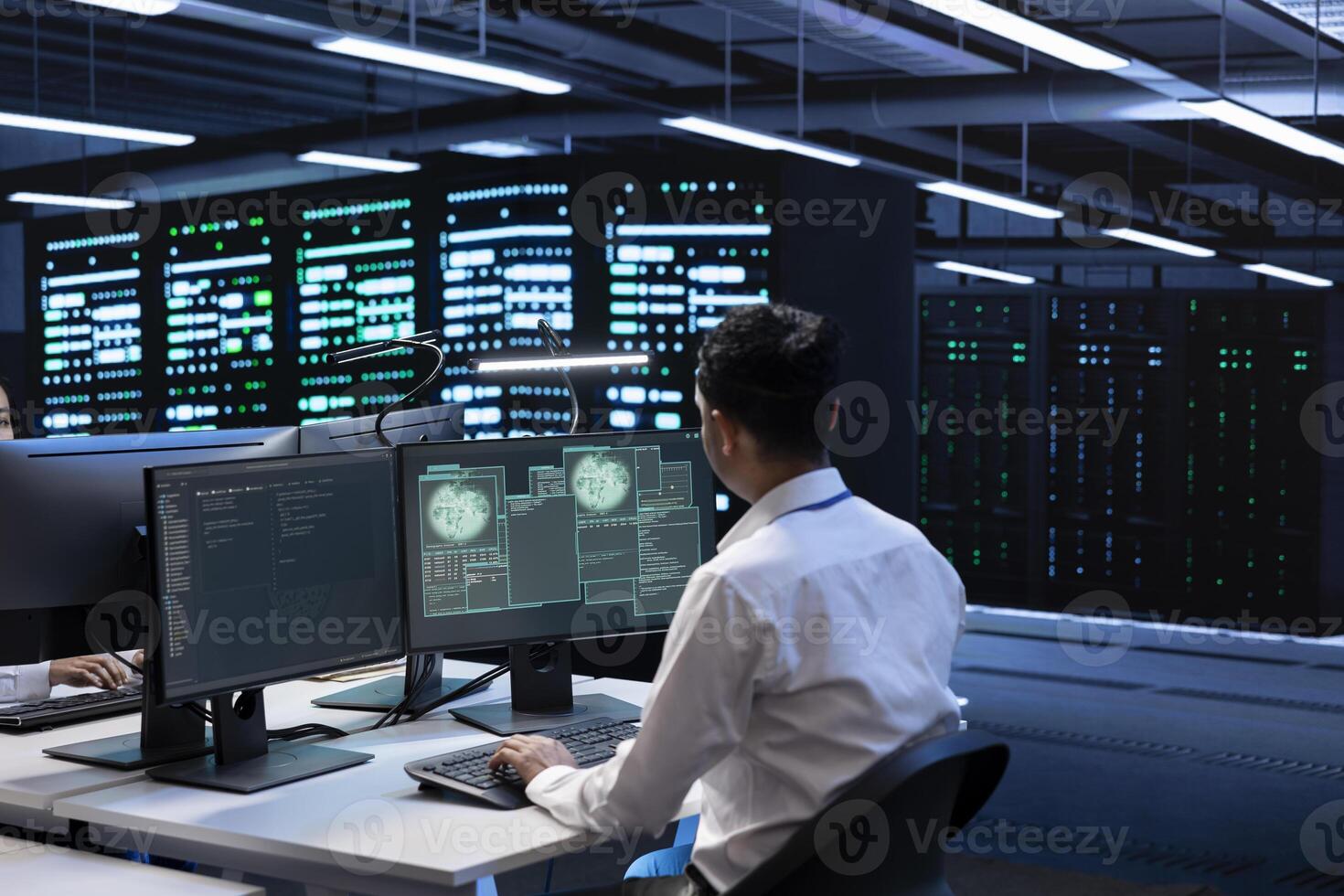 System administrator using computer in server room to support global connections using their hardware. Employee inspecting data center equipment supporting worldwide network using PC photo