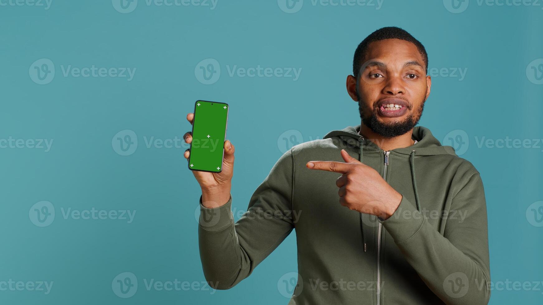 Portrait of african american man doing influencer marketing using green screen phone, studio background. BIPOC person holding empty copy space mockup smartphone device, camera A photo