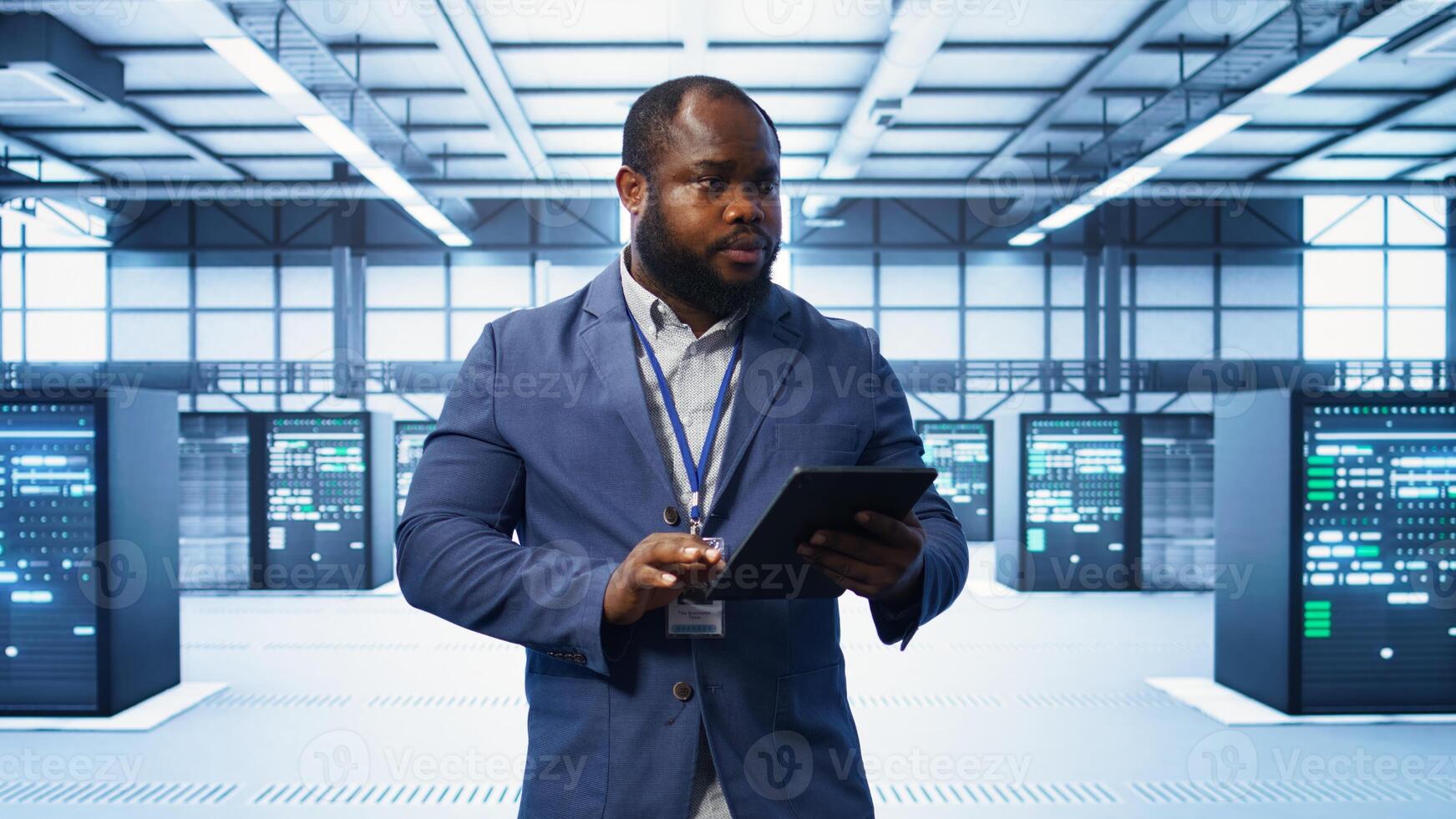 IT technician walking in data center, overseeing server operations using tablet. Expert ensuring optimal performance and data integrity in server hub using digital device, camera B photo
