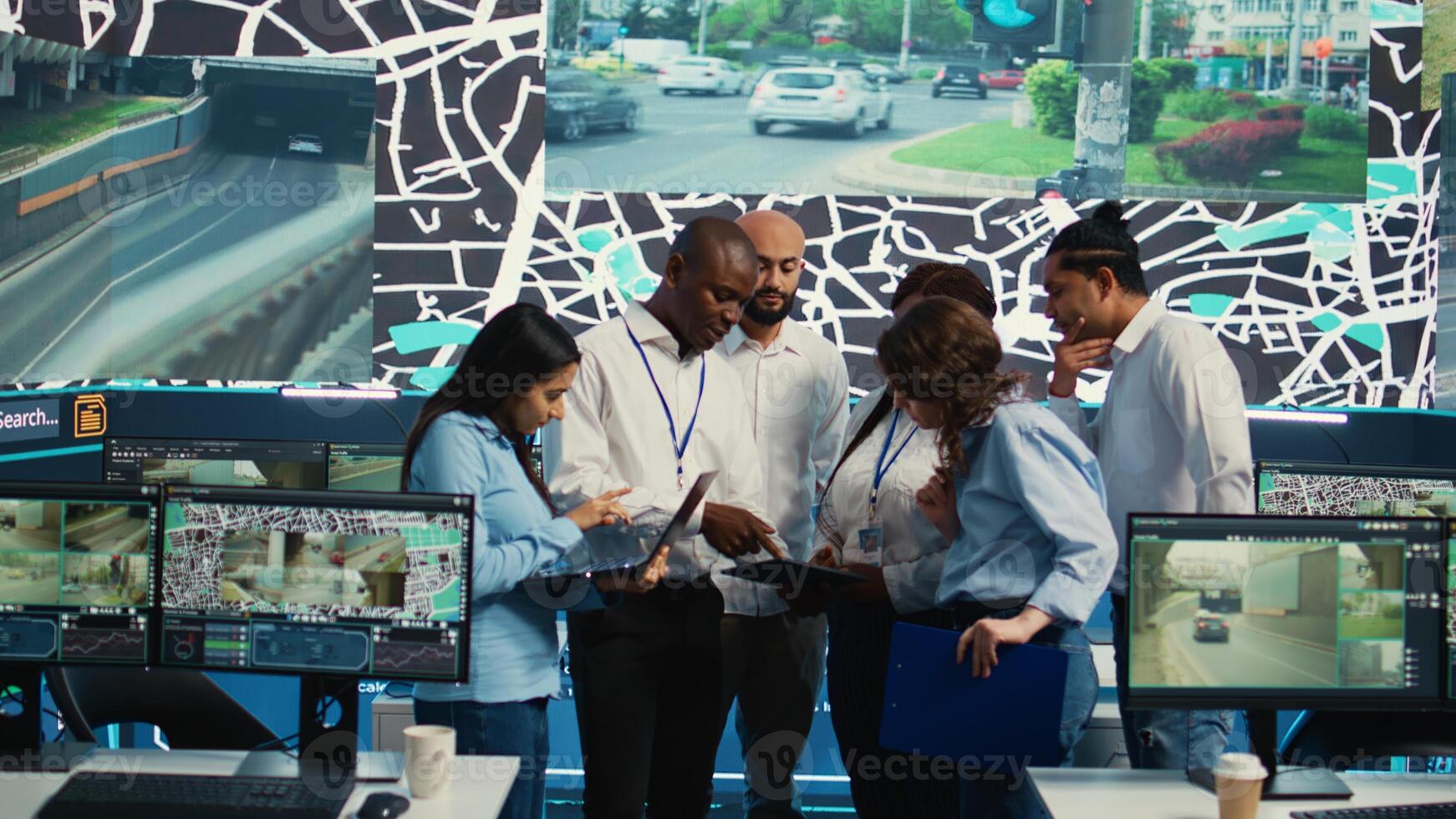 Diverse employees group discussing ways to speed up order delivery, looking for routes to avoid traffic on satellite navigation. Agency operators use CCTV footage in monitoring room. Camera B. photo