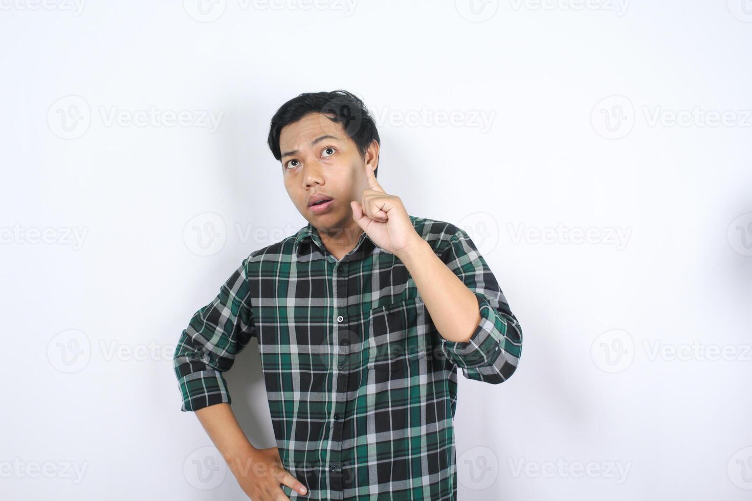 thoughtful asian young man isolated on white background thinking an idea with pointing finger up and looking above photo