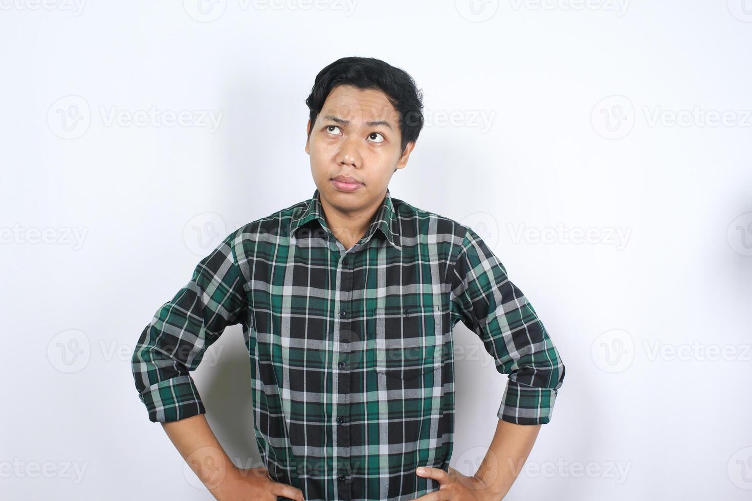 portrait of pensive asian young man looking above with thoughtful expression thinking idea isolated on white background wearing casual plaid shirt photo