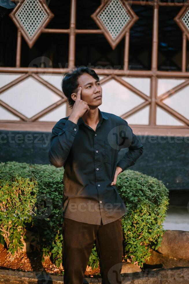 A Southeast Asian man deep in thought, resting his hand on his chin with a contemplative expression photo