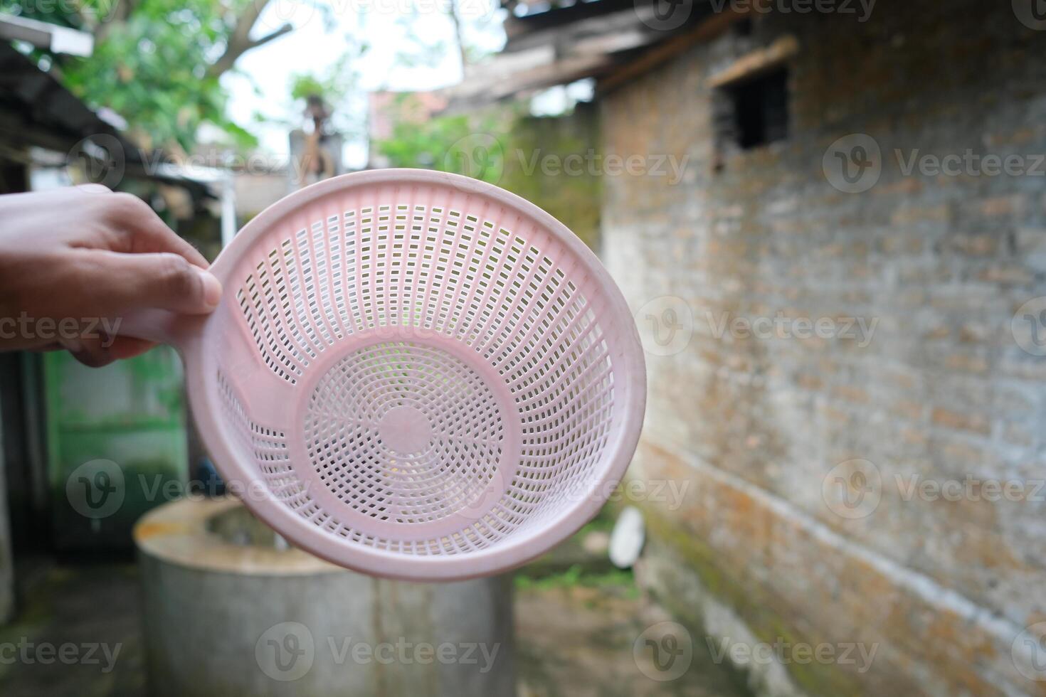 A pink plastic colander held up in a hand in front of a stone wall. photo