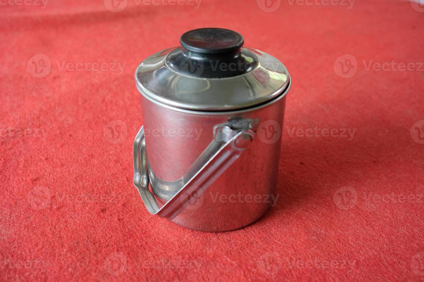 Silver container with a black lid and handle on a red surface. photo