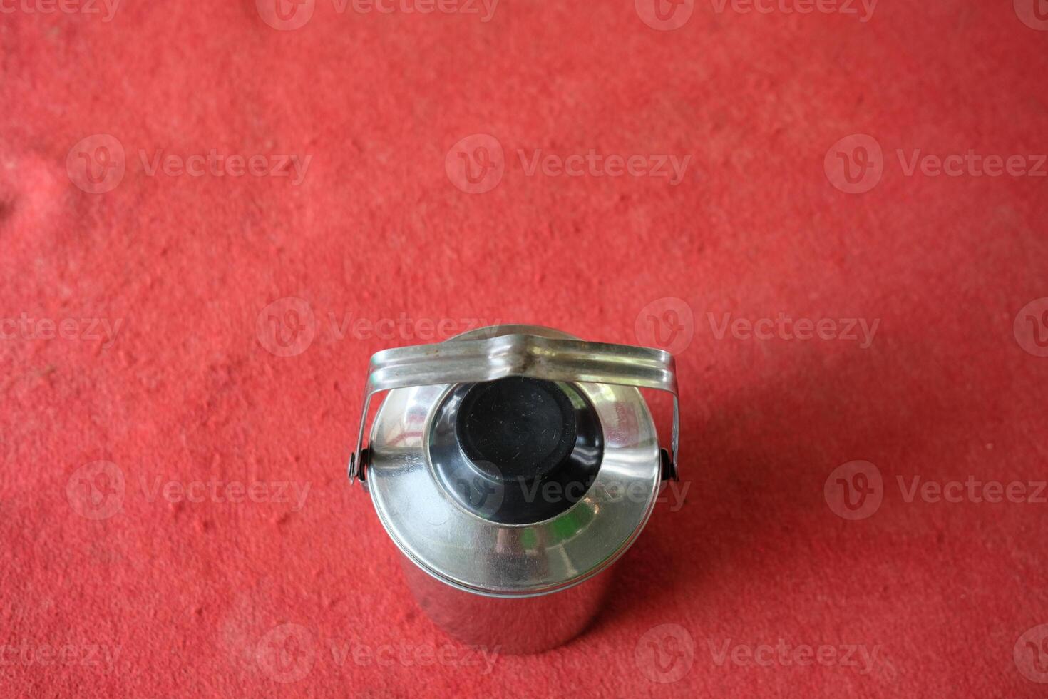 A metallic container with a handle on a red surface. photo