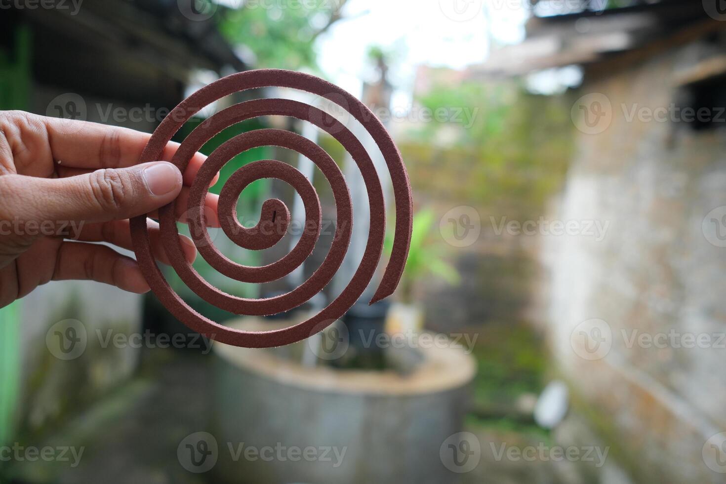 Close-up of a brown mosquito coil held in a hand, with a blurred background of an outdoor setting. photo